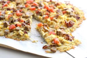 Breakfast pizza with a hash brown crust topped with eggs, bacon and tomatoes