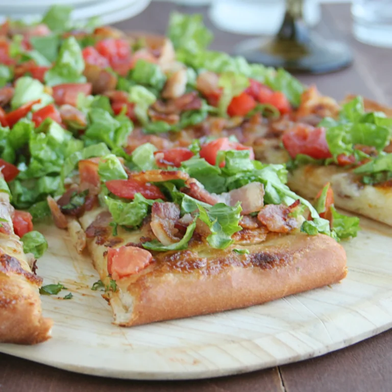 Slices of BLT pizza on a wood serving board topped with shredded lettuce, diced tomatoes, and crumbled Jones Dry Aged Bacon on a golden mayo-brushed crust.