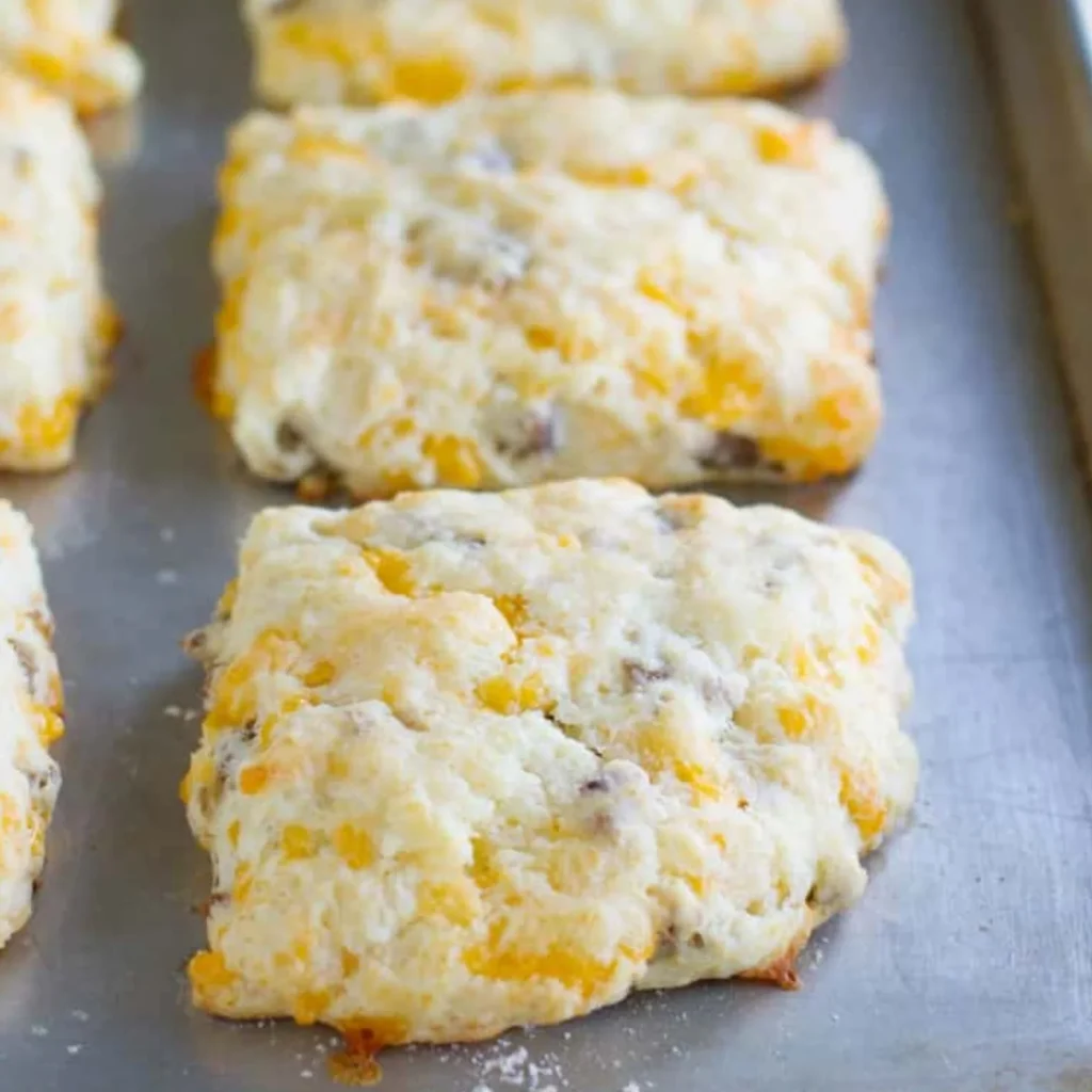 Six golden breakfast sausage and cheese biscuits with visible cheddar and Jones Golden Brown maple sausage throughout, fresh from the oven on a baking sheet.