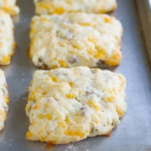 Six golden breakfast sausage and cheese biscuits with visible cheddar and Jones Golden Brown maple sausage throughout, fresh from the oven on a baking sheet.