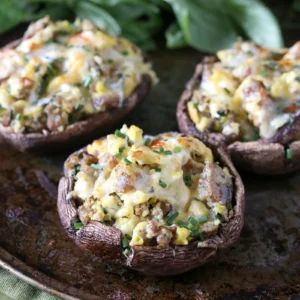 Three portobello mushroom caps stuffed with Jones pork sausage, scrambled eggs, and melted cheddar cheese, garnished with fresh chives, served on a rustic baking pan with fresh basil in the background.