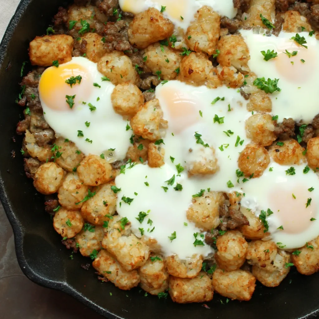 Breakfast tater tot bake in a cast iron skillet with eggs over easy and pork sausage.