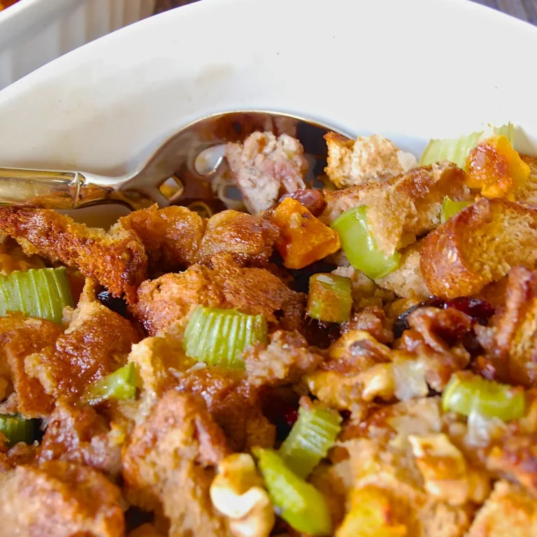 A close-up of butternut squash stuffing with Jones pork sausage, toasted bread cubes, celery, roasted squash, dried cranberries, and walnuts in a white baking …A close-up of butternut squash stuffing with Jones pork sausage, toasted bread cubes, celery, roasted squash, dried cranberries, and walnuts in a white baking dish with a serving spoon.