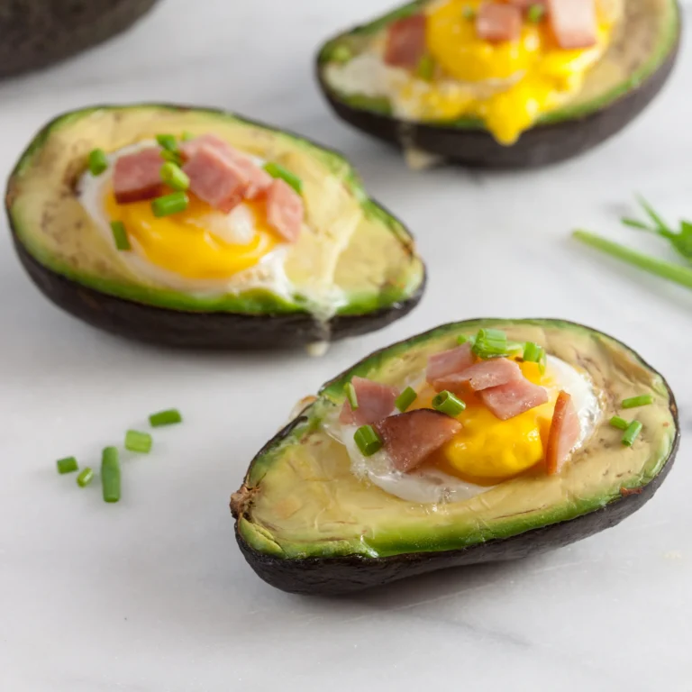 Three baked avocado halves filled with a sunny-side egg, diced Jones Canadian Bacon, and fresh chives, served on a white marble surface.