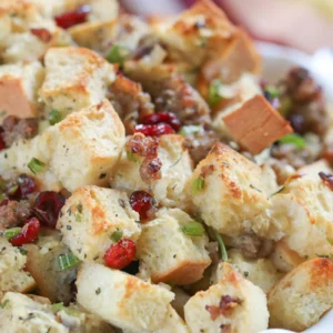 A close-up of cranberry pecan stuffing with toasted French bread cubes, crumbled Jones pork sausage, dried cranberries, fresh herbs, and green onions, baked until golden.