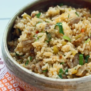 A rustic bowl of dirty rice with chopped Jones Golden Brown All Natural Maple Pork Sausage Links, green chiles, red pepper, scallions, and cilantro seasoned with Cajun spice, served on an orange patterned cloth.