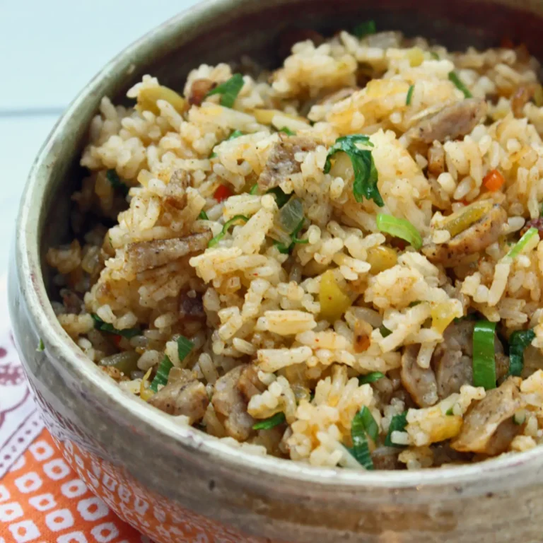 A rustic bowl of dirty rice with chopped Jones Golden Brown All Natural Maple Pork Sausage Links, green chiles, red pepper, scallions, and cilantro seasoned with Cajun spice, served on an orange patterned cloth.