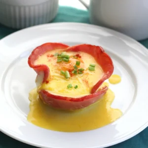 A Jones Canadian Bacon breakfast cup with a baked egg inside, drizzled with hollandaise sauce and garnished with fresh chives and paprika, served on a white plate.