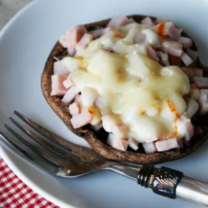 A grilled portabella mushroom cap filled with diced Jones Breakfast Ham and topped with melted Muenster cheese, served in a white bowl with a fork and a red checked cloth.