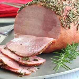A sliced Jones Dairy Farm Uncured Heritage Half Ham coated in a fresh rosemary, garlic, and cracked pepper crust, served on a silver platter with fresh rosemary sprigs.