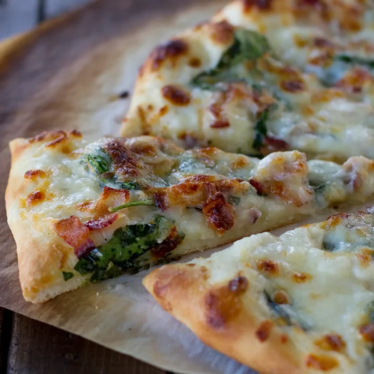 Slices of spinach bacon ranch pizza with melted mozzarella, crispy Jones Dry Aged Bacon, and fresh spinach on a golden baked crust, served on parchment paper on a wood surface.