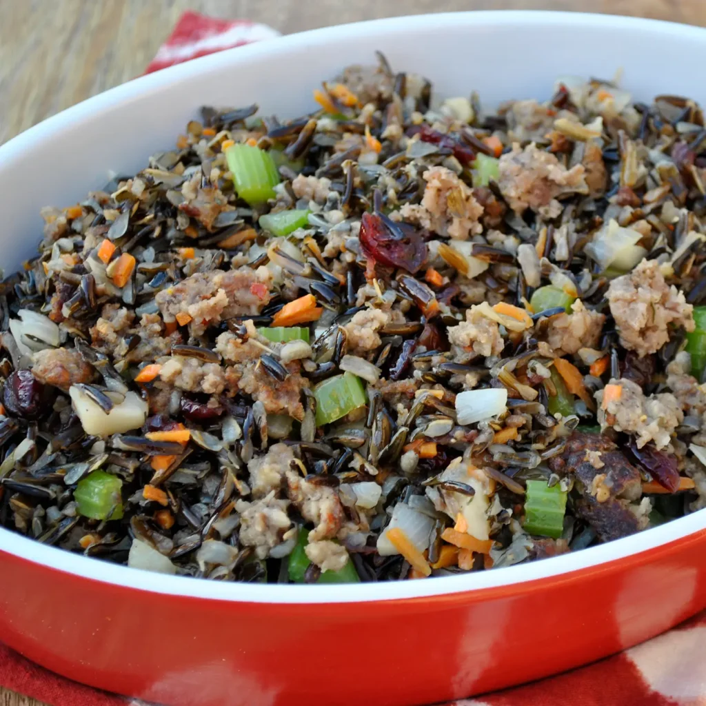 10:21 AMClaude responded: A red baking dish filled with wild rice and water chestnut stuffing with Jones pork sausage, dried cranberries, celery, carrots, and onion, served on a wood su…A red baking dish filled with wild rice and water chestnut stuffing with Jones pork sausage, dried cranberries, celery, carrots, and onion, served on a wood surface with a red and white cloth.