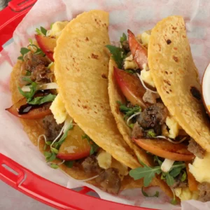 11:52 AMClaude responded: Four corn tortilla breakfast tacos filled with Jones pork sausage, scrambled eggs, charred peach slices, microgreens, shredded cheese, and a drizzle of honey b…Four corn tortilla breakfast tacos filled with Jones pork sausage, scrambled eggs, charred peach slices, microgreens, shredded cheese, and a drizzle of honey balsamic glaze, served in a red basket.