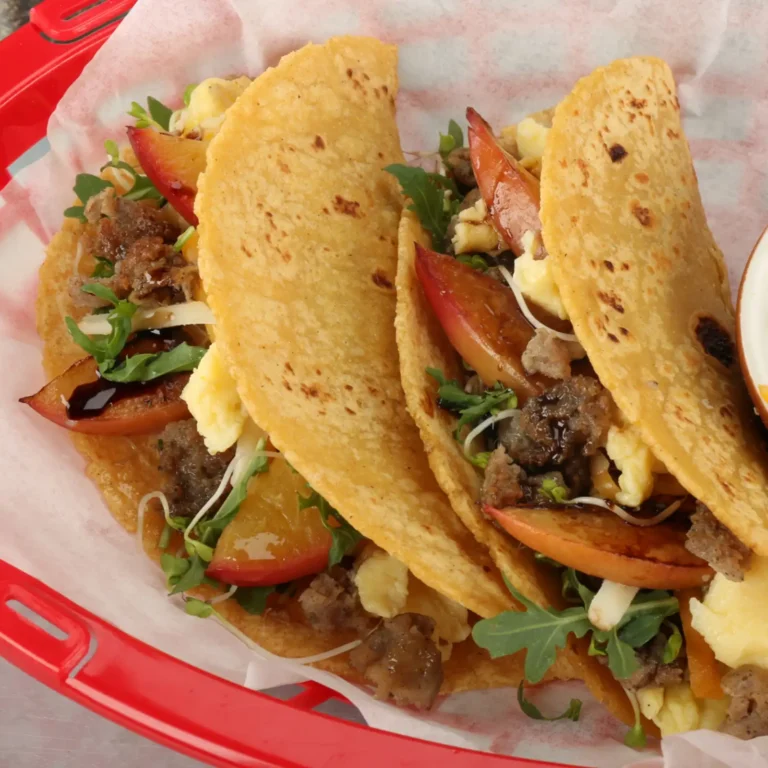 11:52 AMClaude responded: Four corn tortilla breakfast tacos filled with Jones pork sausage, scrambled eggs, charred peach slices, microgreens, shredded cheese, and a drizzle of honey b…Four corn tortilla breakfast tacos filled with Jones pork sausage, scrambled eggs, charred peach slices, microgreens, shredded cheese, and a drizzle of honey balsamic glaze, served in a red basket.