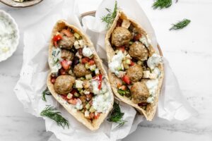 Two pitas filled with chicken meatballs, tomatoes, cucumbers, and tzatziki.