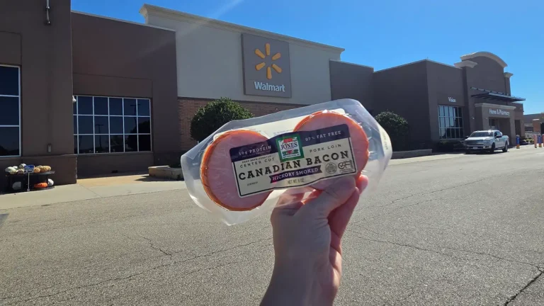 A hand holds a 6 oz. package of Jones Hickory Smoked Canadian Bacon in front of a Walmart store entrance.