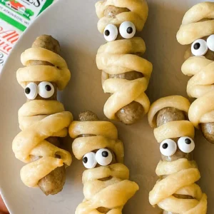 Five mummy-wrapped Jones sausage links with dough strips and candy eyes, served on a white plate