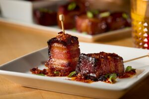 Two Hot Honey and Chile Glazed Bacon Bites on a plate, foodservice recipe idea, bacon slab