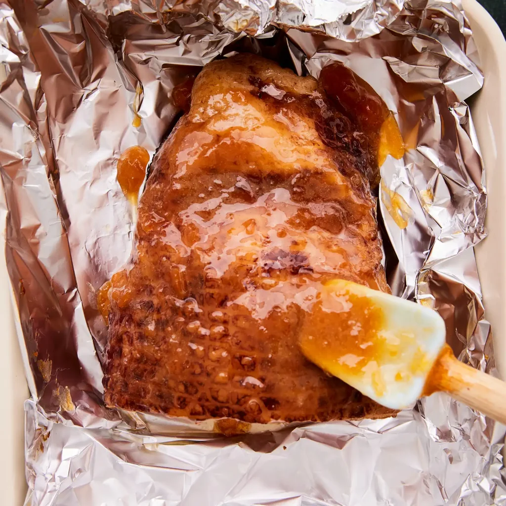 Whole glazed ham roasting in a Dutch oven lined with foil.