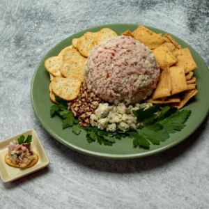 Jones Canadian bacon date cheeseball coated in diced Canadian bacon and blue cheese crumbles, served on a green platter with assorted crackers, toasted pecans, and fresh parsley
