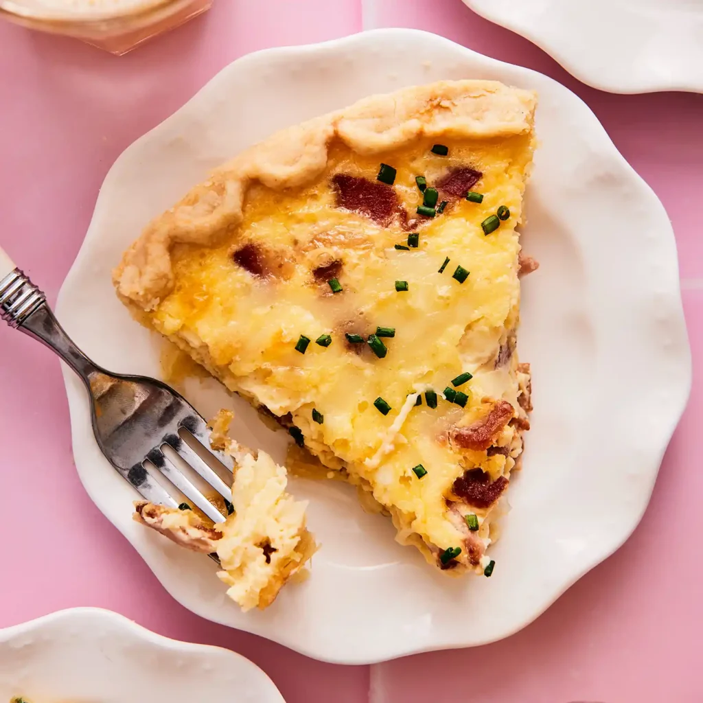 A slice of Jones Dairy Farm Quiche Lorraine with crispy bacon and Gruyere on a white plate, garnished with fresh chives