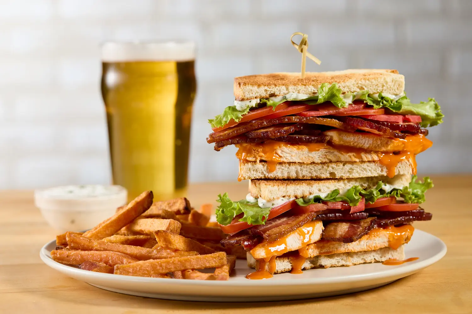 Buffalo chicken club sandwich with bacon, lettuce, and tomato, served with sweet potato fries