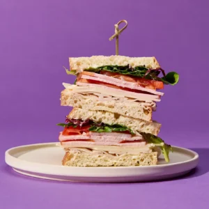 Stacked sandwich with Jones Dairy Farm Canadian bacon, cheese, tomato, and mixed greens on white bread