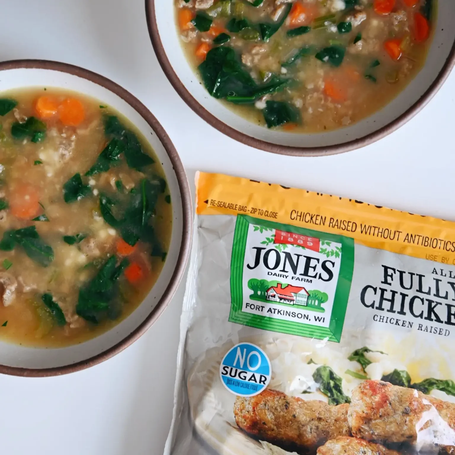 Two bowls of gluten-free Italian wedding soup made with Jones fully cooked chicken sausage, spinach, and carrots, served alongside the bulk product package