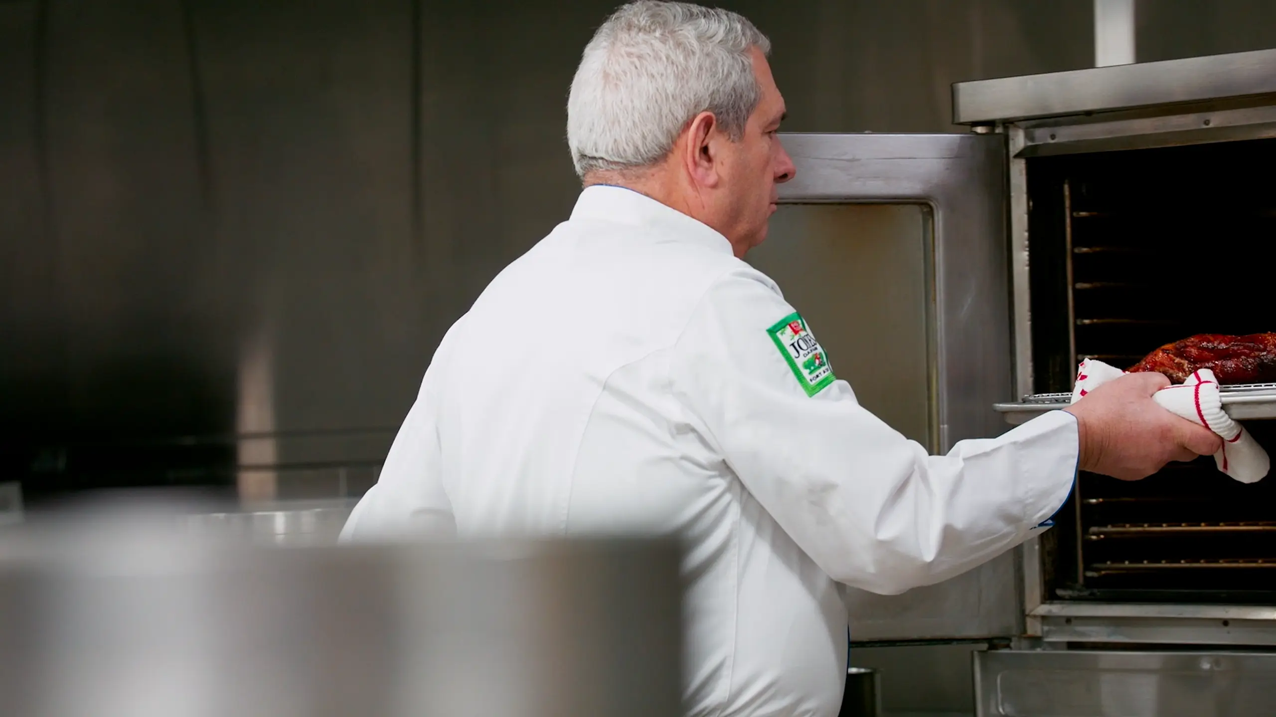 Chef John Coletta pulling slab bacon from a commercial oven in a professional kitchen