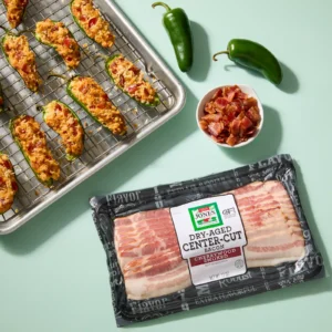 Jones Dairy Farm Dry Aged Cherrywood Smoked Bacon package with bacon jalapeño poppers on a sheet pan
