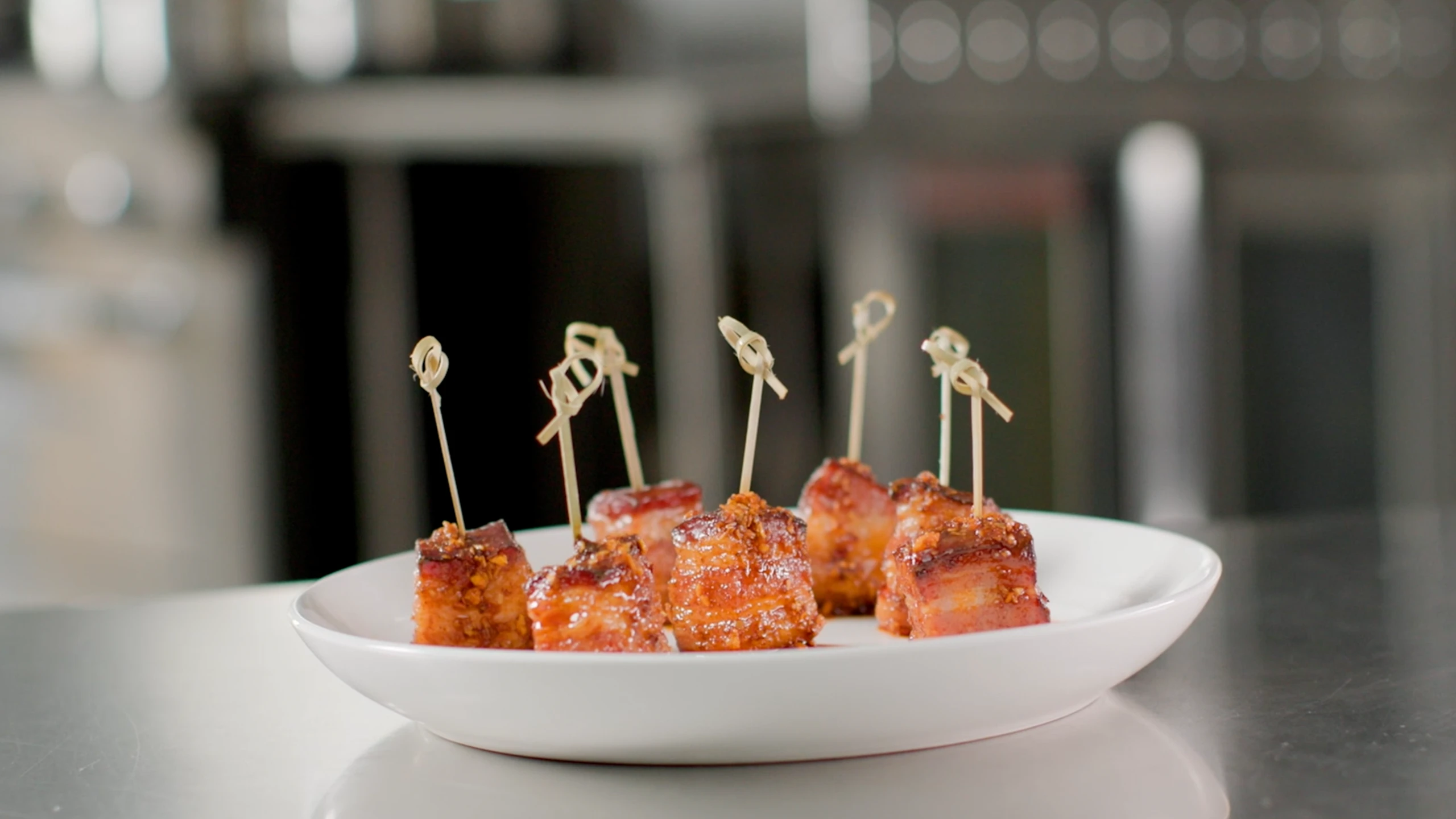 Jones Dairy Farm glazed bacon bites on toothpicks served on a white plate in a commercial kitchen
