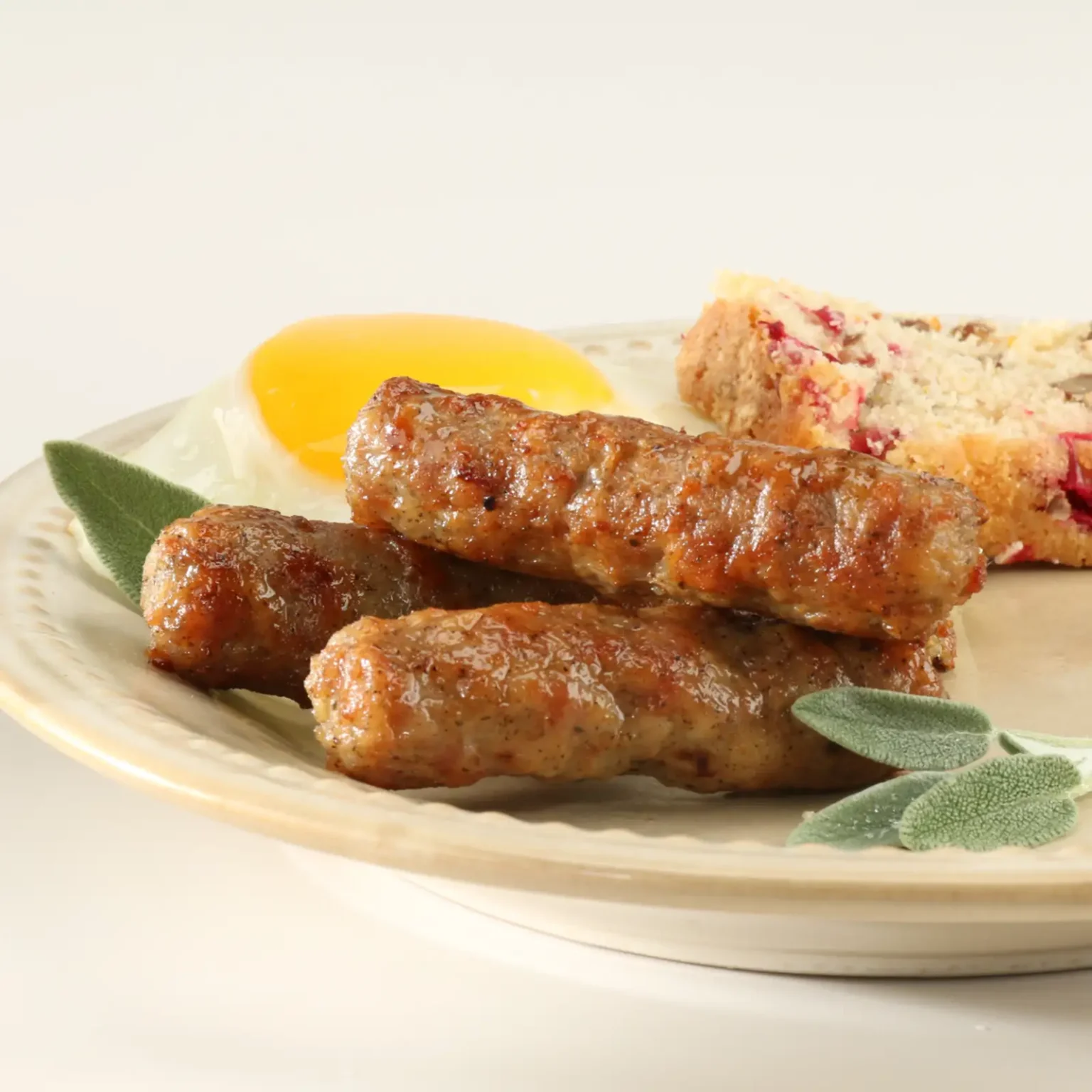 Jones No Antibiotics Ever pork sausage links served on a plate with a fried egg, fresh sage, and cranberry bread