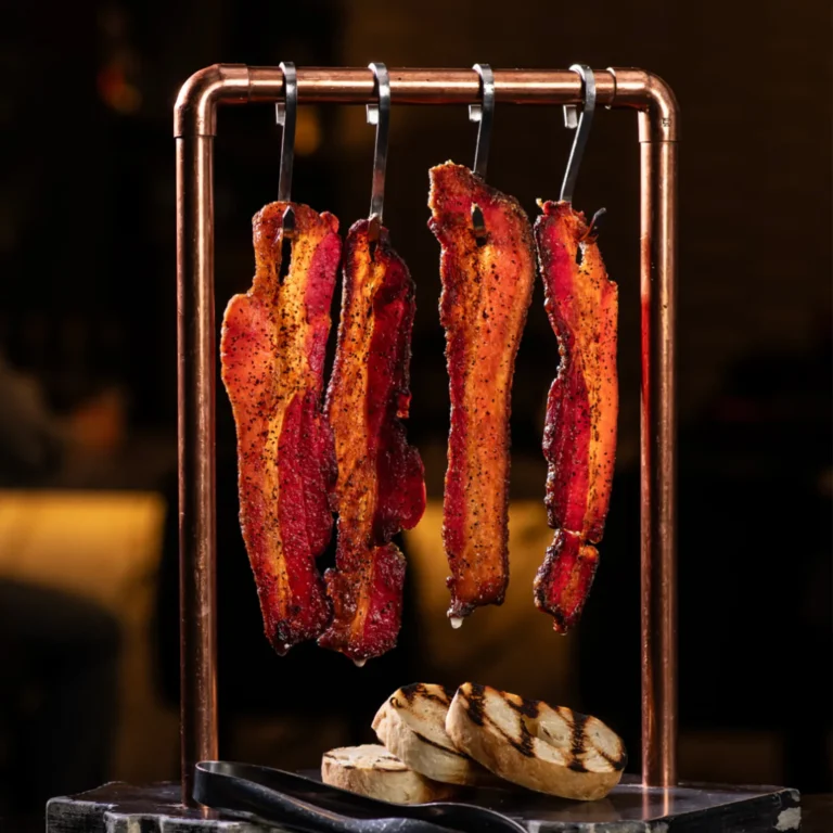 Jones Dairy Farm Dry Aged Bacon hangs above grilled baguette slices in an appetizer dish.