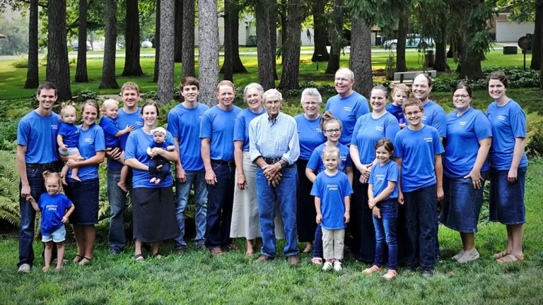 A multigenerational Wholestone Farms family poses outdoors in matching blue Wholestone Farms T-shirts on a grassy lawn surrounded by trees.