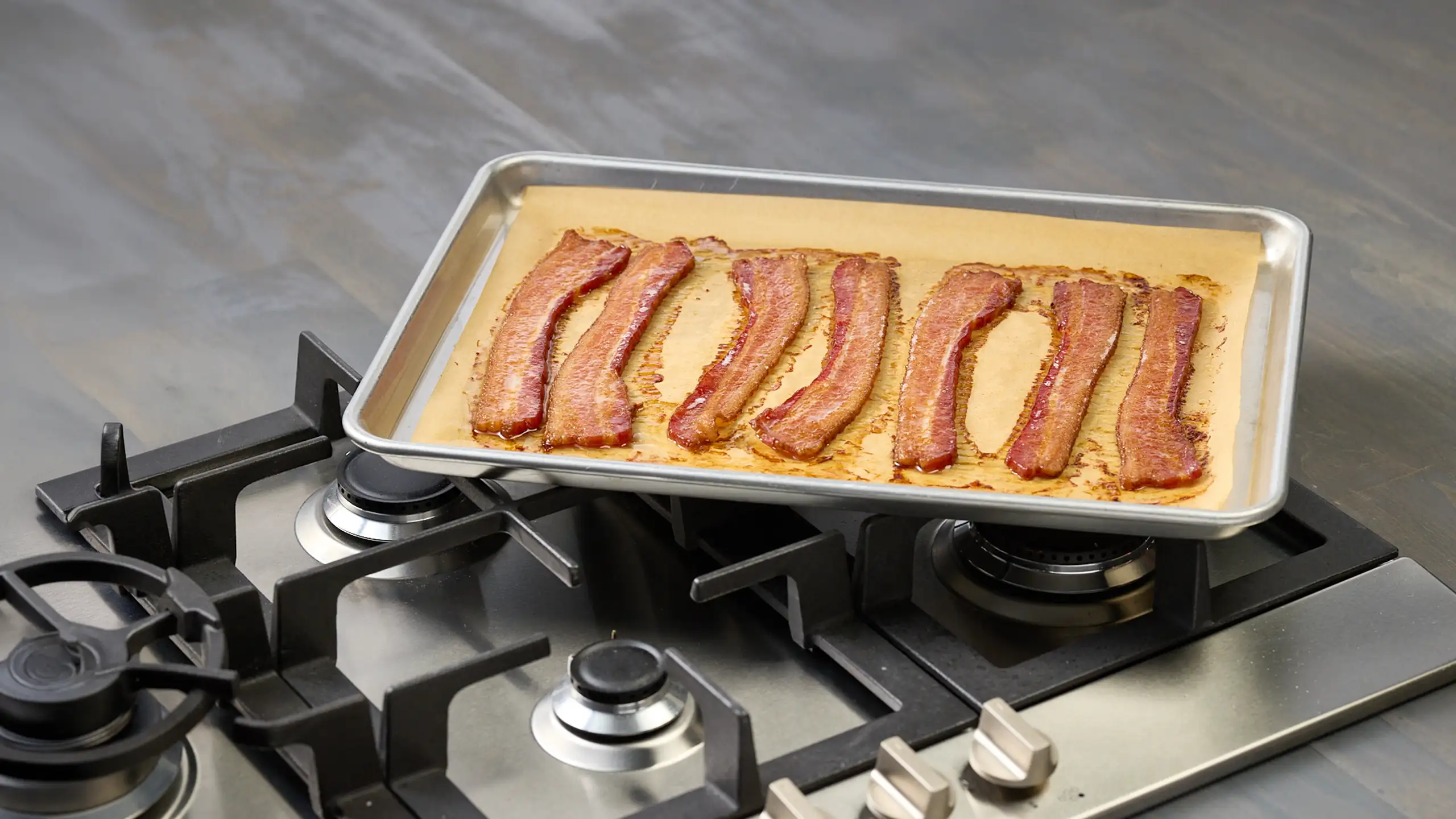 Jones Dairy Farm bacon strips laid out on a parchment-lined sheet pan on a gas stovetop, ready to go in the oven