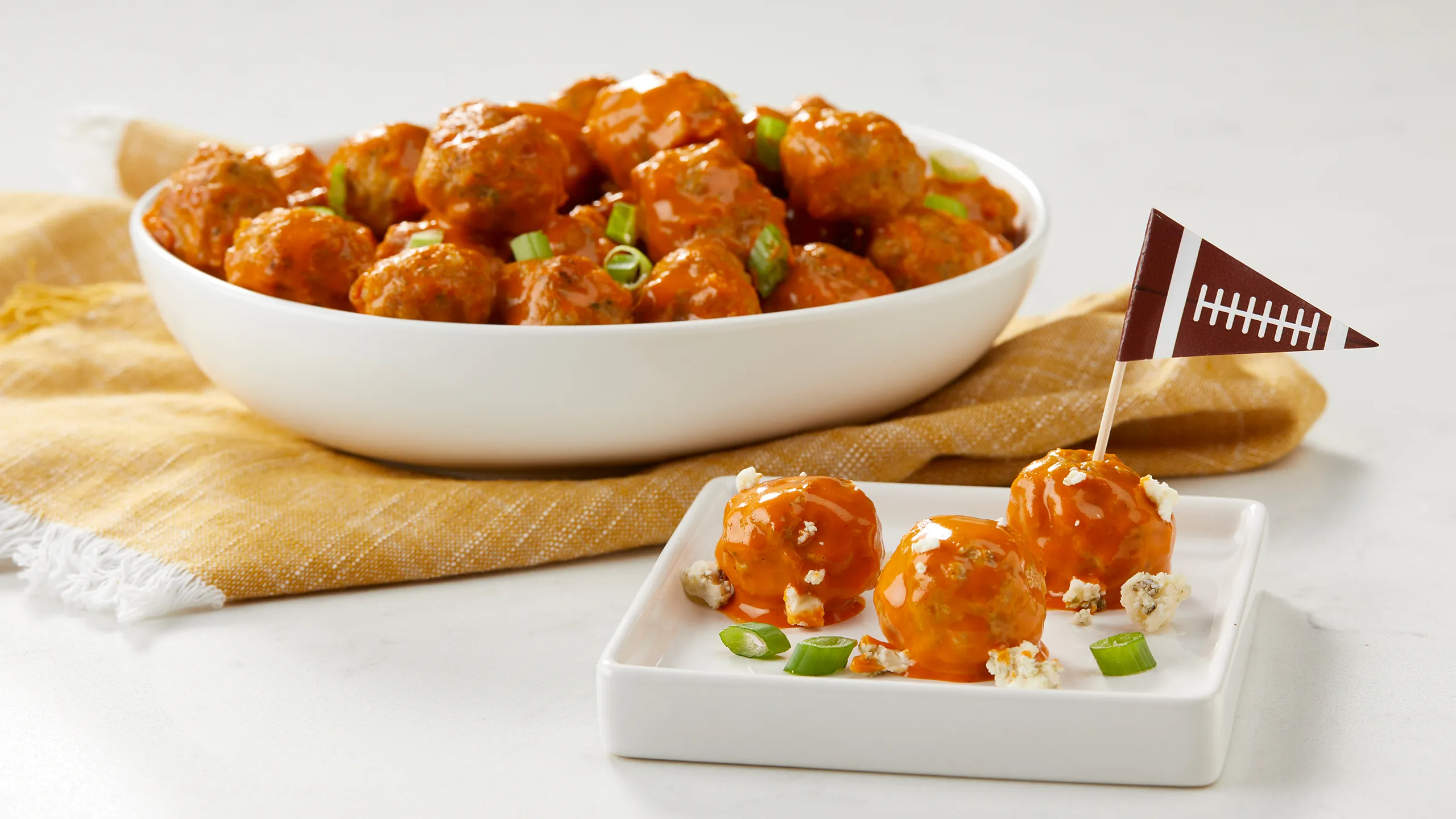 Jones Dairy Farm all natural chicken meatballs tossed in buffalo sauce with crumbled blue cheese and sliced scallions, served as a game day appetizer with a football pennant pick