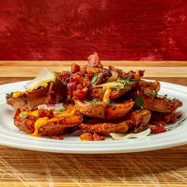 Bacon Smashed Sweet Potatoes piled on a white plate with crispy Jones Raw Diced Bacon lardons, gochujang mayo drizzle, shaved Pecorino Romano, and fresh herbs