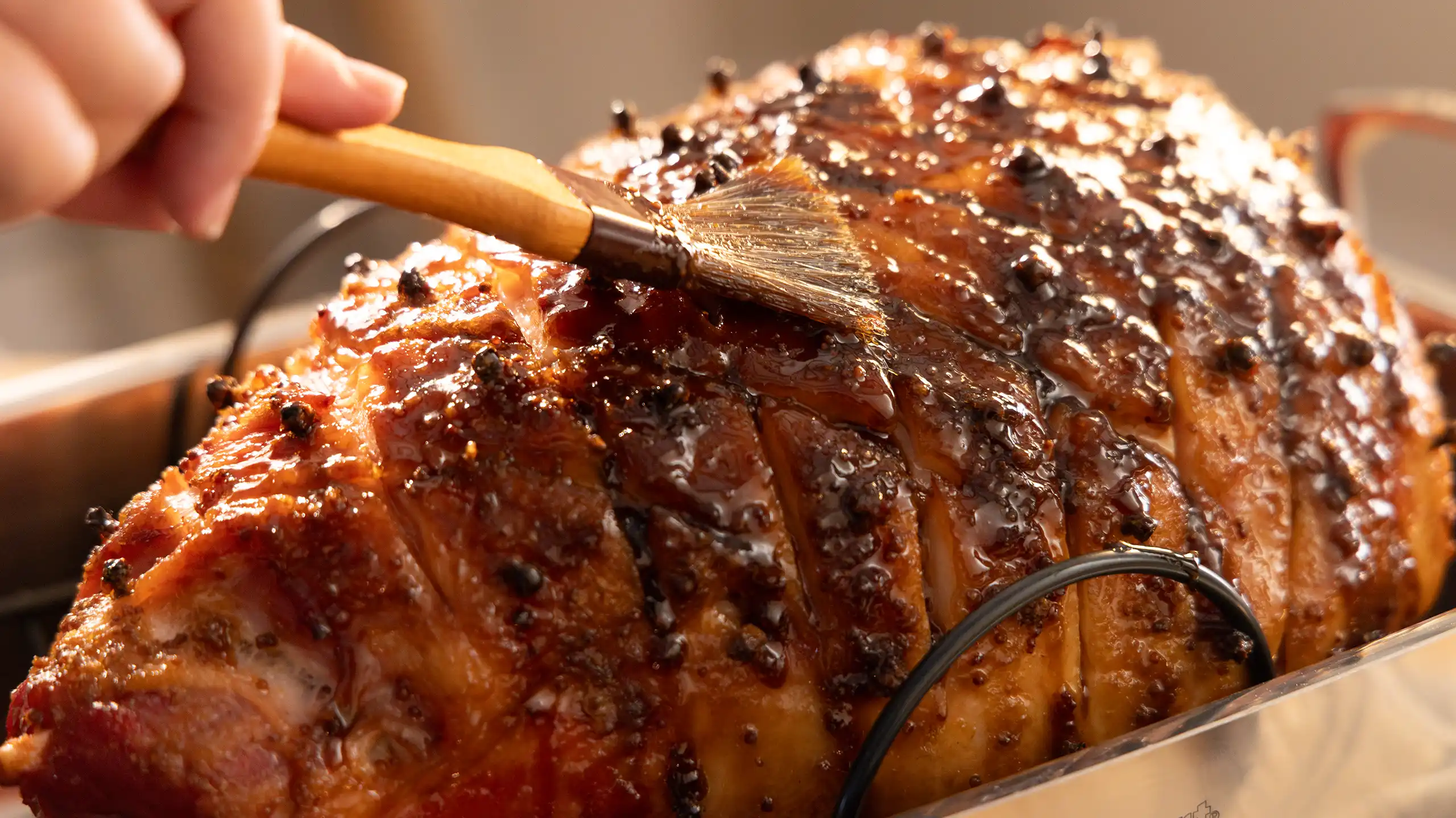 Hand basting glaze onto a Jones bone-in ham studded with whole cloves in a roasting pan