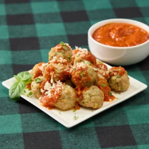 Jones Dairy Farm chicken meatballs topped with marinara sauce, grated Parmesan, and fresh herbs, served on a white square plate with a bowl of marinara and a fresh basil garnish on a green buffalo check tablecloth