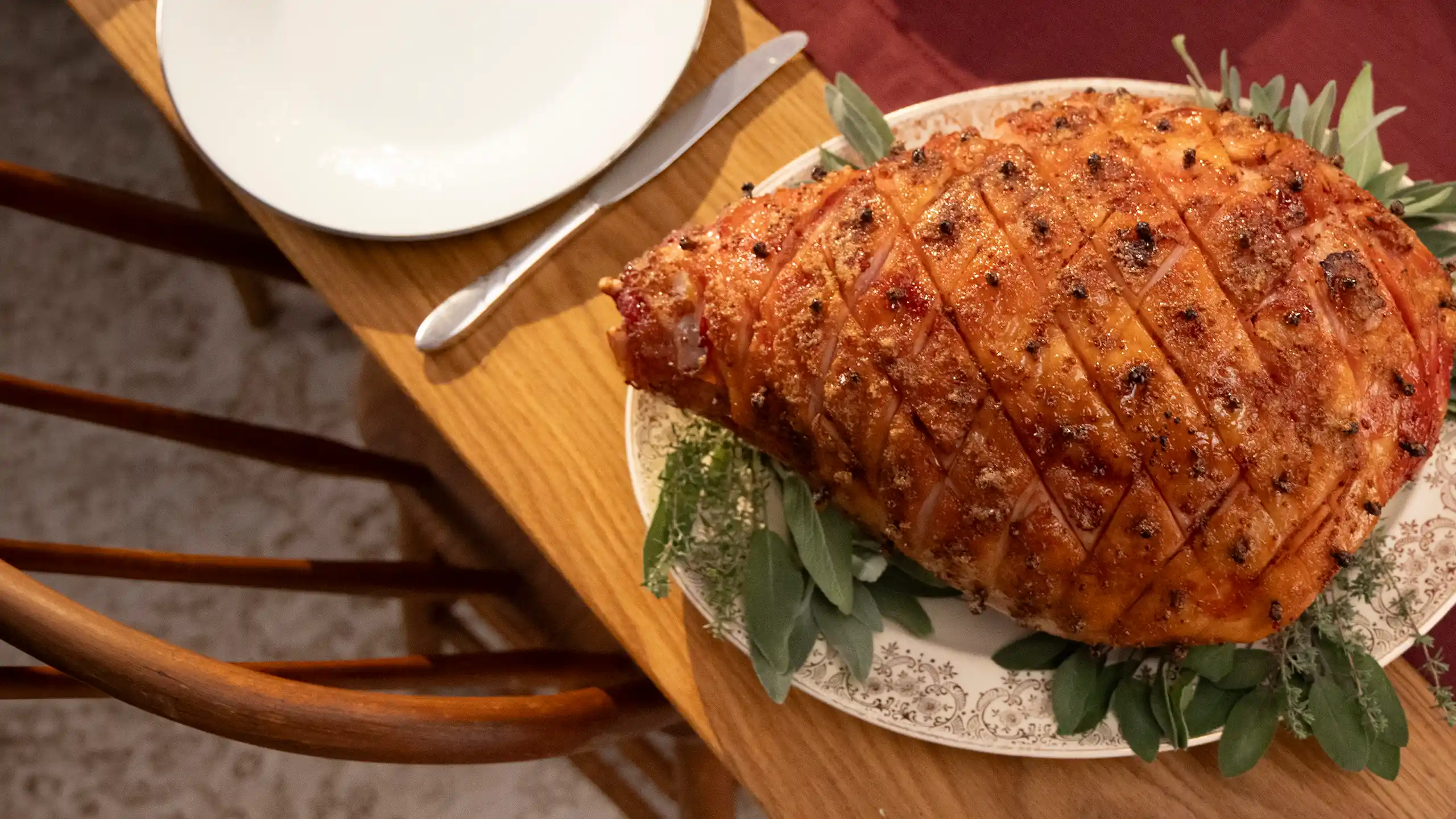Jones Bone-In Ham scored and studded with whole cloves on a decorative platter with fresh sage and herb garnish, plated for a holiday or banquet table setting