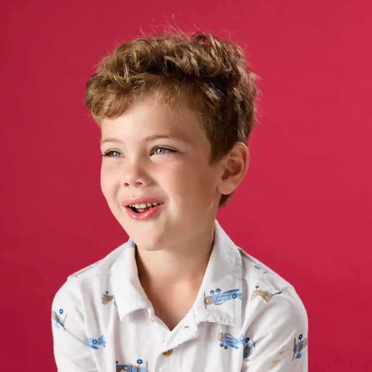 Smiling young boy in a white button-down shirt against a red background.