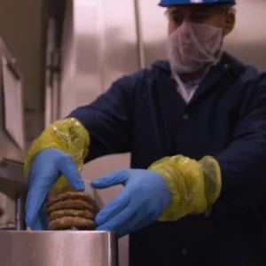 A Jones Dairy Farm team member in safety gear handling sausage patties on the production floor in Fort Atkinson, Wisconsin