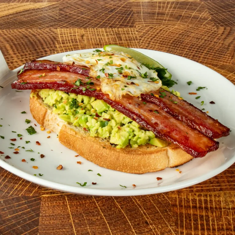 Jones Dairy Farm cherrywood smoked dry aged bacon strips on avocado toast with a fried egg, fresh cilantro, red pepper flakes, and a lime wedge.