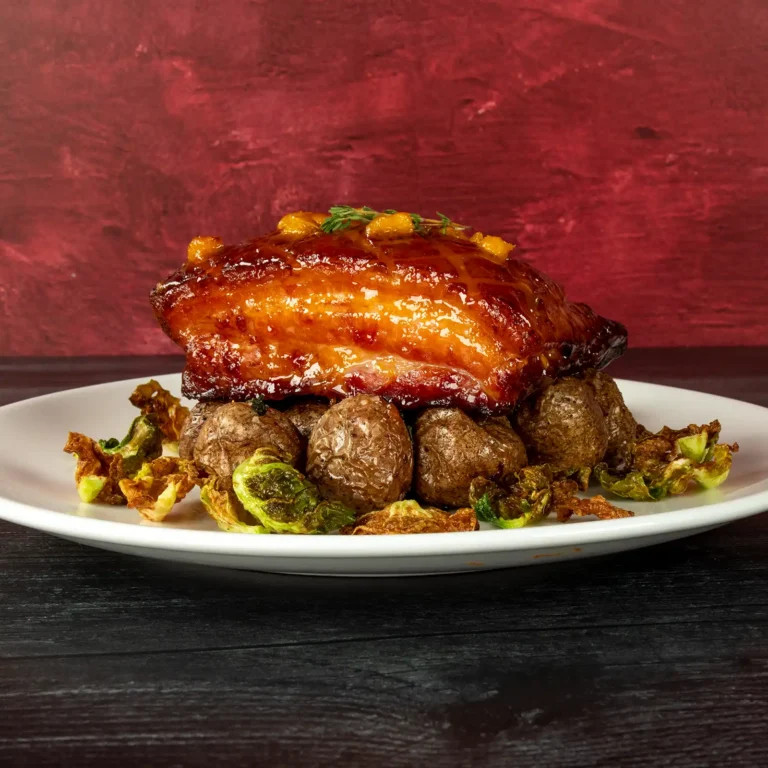 Jones Dairy Farm cherrywood smoked dry aged slab bacon steak with a fruit glaze and fresh thyme, plated over roasted baby potatoes and crispy Brussels sprouts.