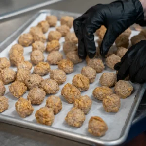 2:08 PMClaude responded: Gloved hands arrange rows of Jones Dairy Farm chicken meatballs on a parchment-lined sheet pan in a commercial kitchenGloved hands arrange rows of Jones Dairy Farm chicken meatballs on a parchment-lined sheet pan in a commercial kitchen