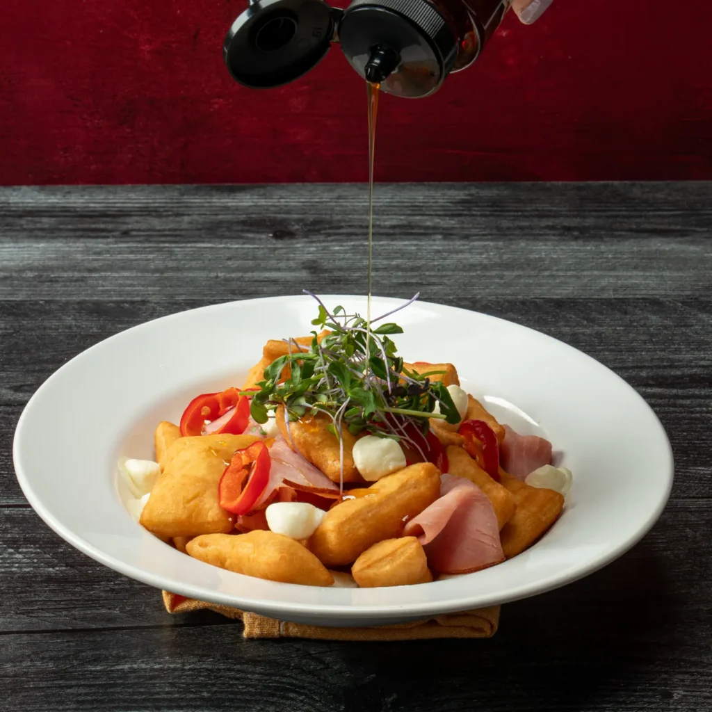 Jones Deli Sliced Ham and golden fried gnocco fritto with fresh mozzarella pearls, sweet red peppers, and microgreens with hot honey being drizzled over the top