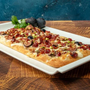 Maple Bacon Flatbread topped with whipped burrata, caramelized shallots, maple glazed figs, crushed pistachios, and candied Jones Raw Diced Bacon on a white serving platter