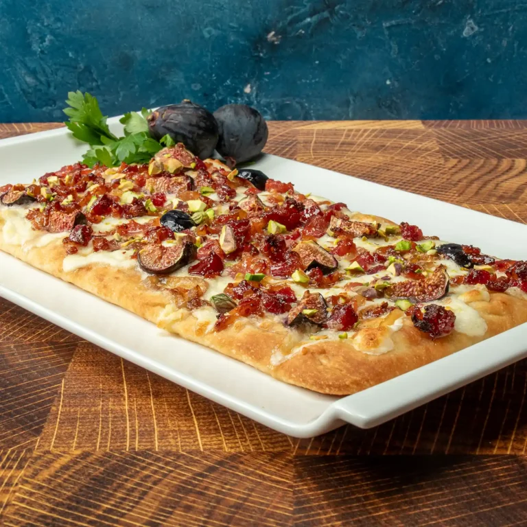 Maple Bacon Flatbread topped with whipped burrata, caramelized shallots, maple glazed figs, crushed pistachios, and candied Jones Raw Diced Bacon on a white serving platter