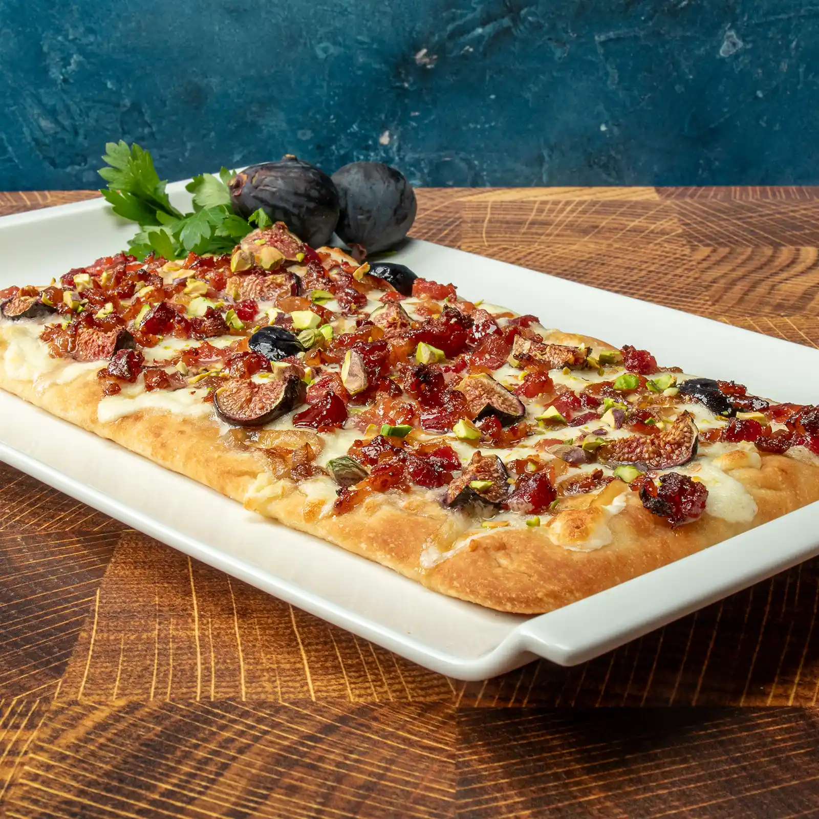 Maple Bacon Flatbread topped with whipped burrata, caramelized shallots, maple glazed figs, crushed pistachios, and candied Jones Raw Diced Bacon on a white serving platter