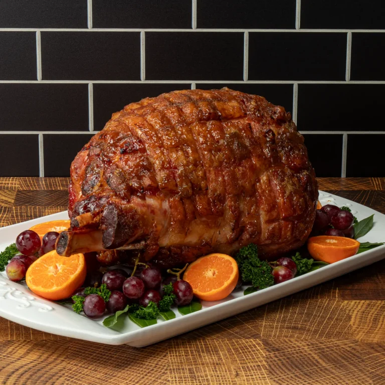 Jones Bone-In Ham scored and glazed, plated with fresh cranberries, orange slices, and herbs on a white serving platter